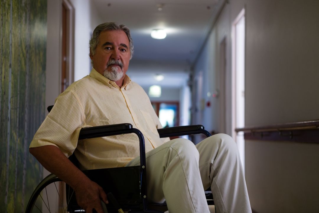 Portrait of senior man sitting on wheelchair in corridor - Free Images, Stock Photos and Pictures on Pikwizard.com