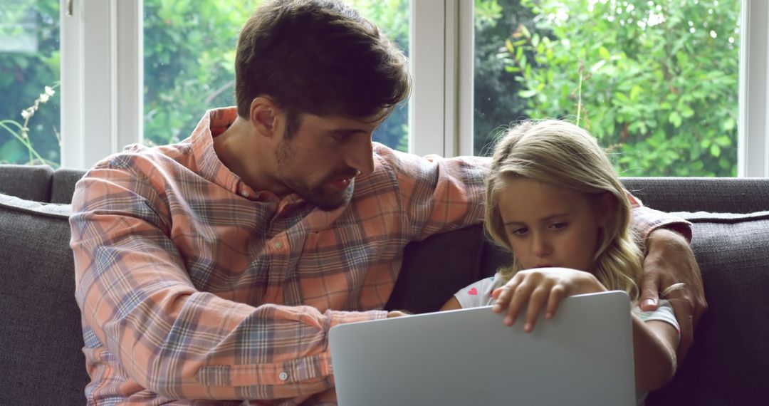 Father Helping Young Daughter with Laptop on Couch Home Learning - Free Images, Stock Photos and Pictures on Pikwizard.com