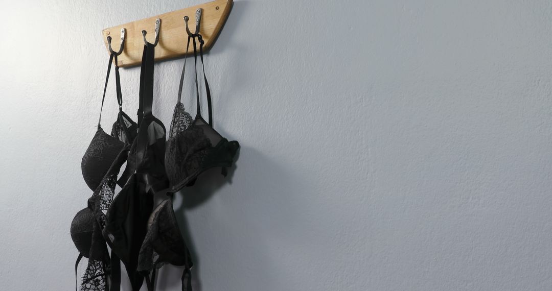 Several black bras hang from hooks on a wooden rack against a white wall, with copy space - Free Images, Stock Photos and Pictures on Pikwizard.com