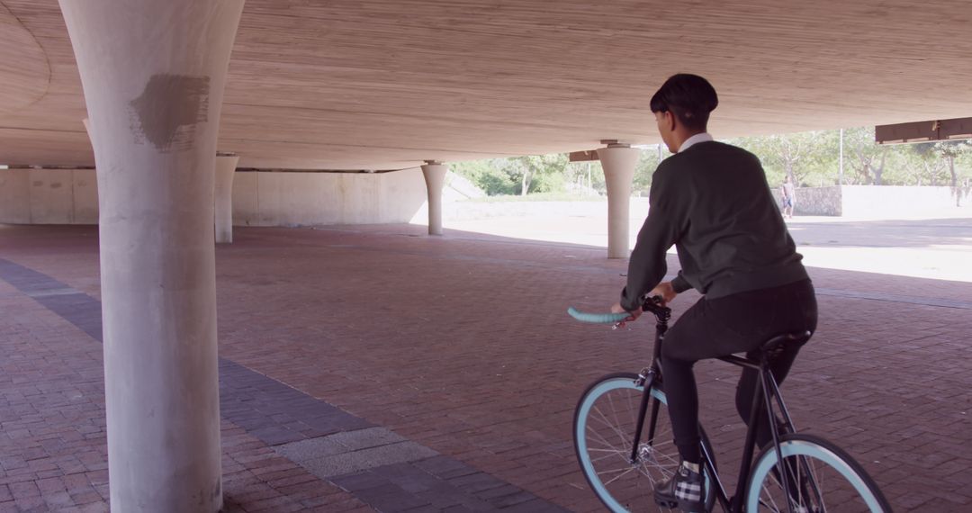 Person Riding Bicycle Under Modern Structure in Urban Landscape - Free Images, Stock Photos and Pictures on Pikwizard.com