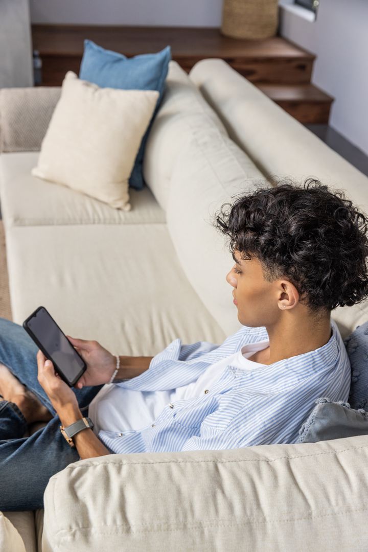 Young Man Relaxing on Sofa Using Smartphone and Wearing Smartwatch