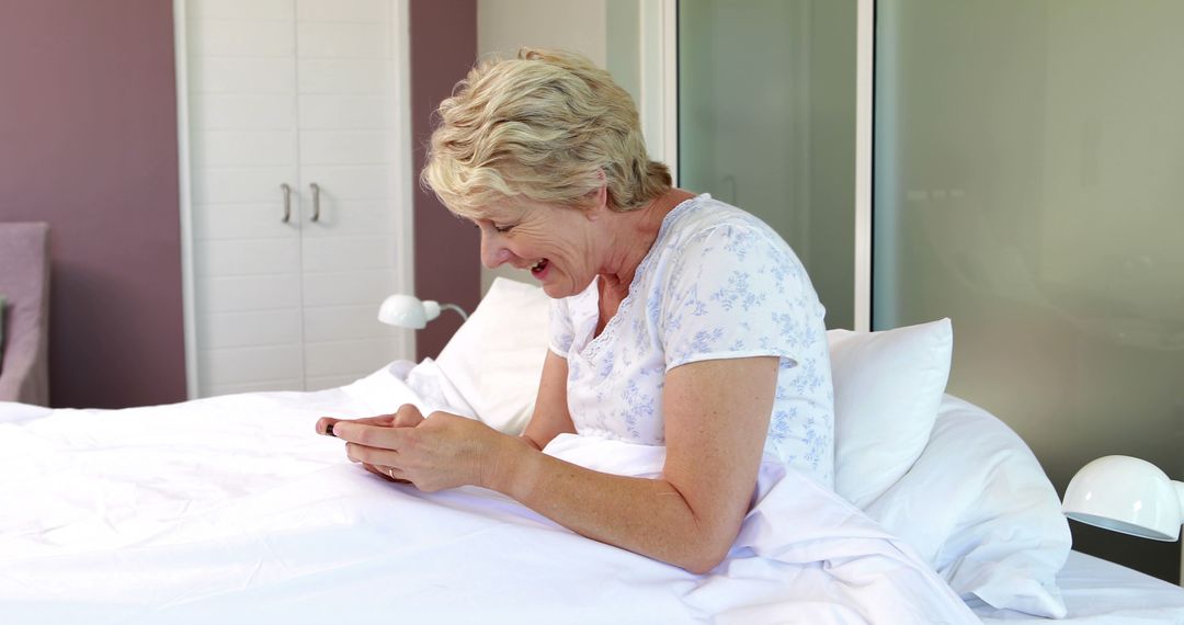 Senior Woman Laughing While Using Smartphone in Bed - Free Images, Stock Photos and Pictures on Pikwizard.com