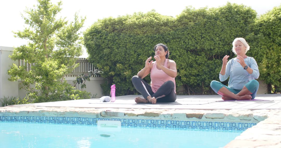 Two Women Meditating by Pool on Wooden Deck with Greenery - Free Images, Stock Photos and Pictures on Pikwizard.com