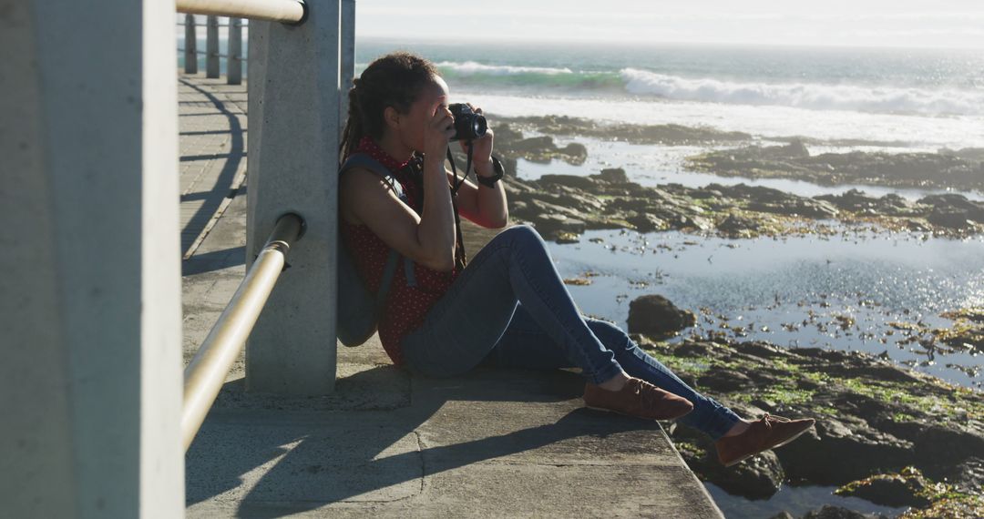 Woman photographing seashore sitting on concrete platform - Free Images, Stock Photos and Pictures on Pikwizard.com