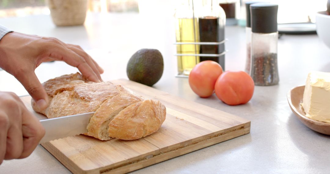 Hand Slicing Fresh Bread with Avocado and Tomato in Kitchen