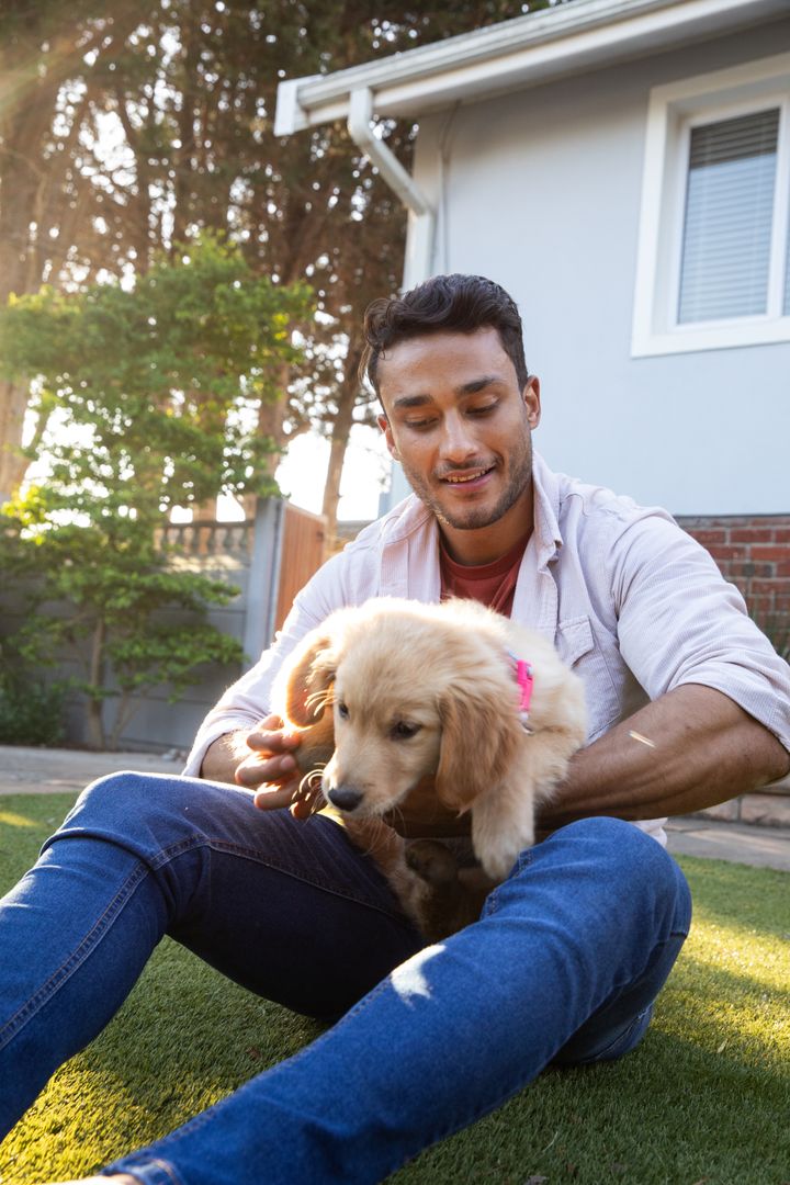 Smiling Man Enjoying Playtime with Golden Puppy on Lawn Outdoors