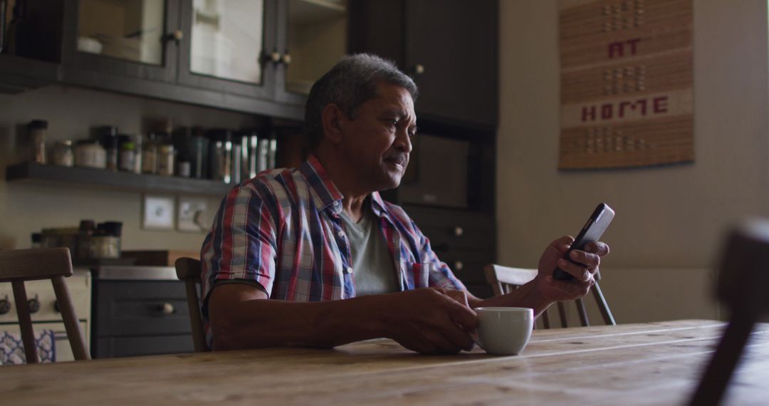 Mature Man Drinking Coffee While Using Smartphone at Kitchen Table - Free Images, Stock Photos and Pictures on Pikwizard.com