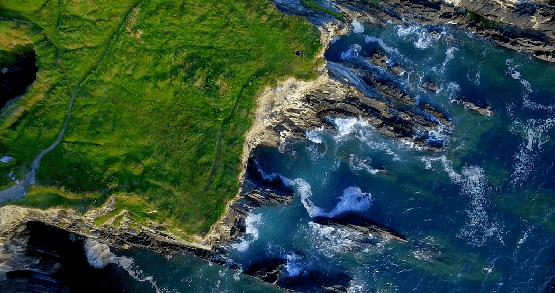 Transparent Waves Crashing against Rugged Cliffs and Lush Greenery