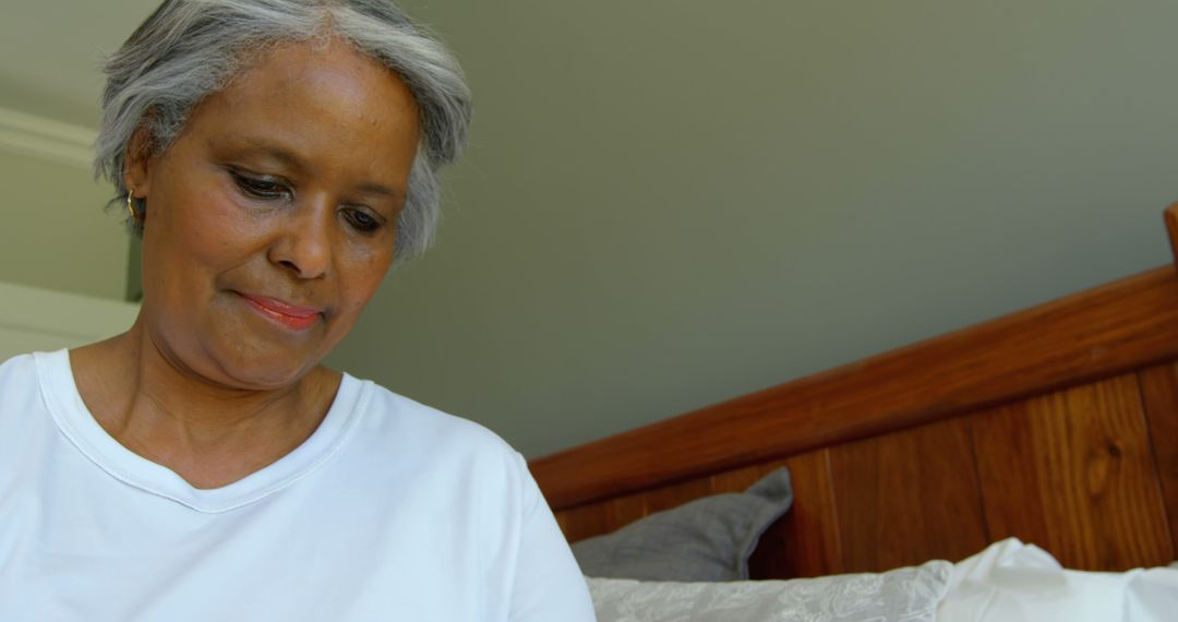 Elderly Woman Smiling While Sitting on Bed in Tranquil Bedroom - Free Images, Stock Photos and Pictures on Pikwizard.com