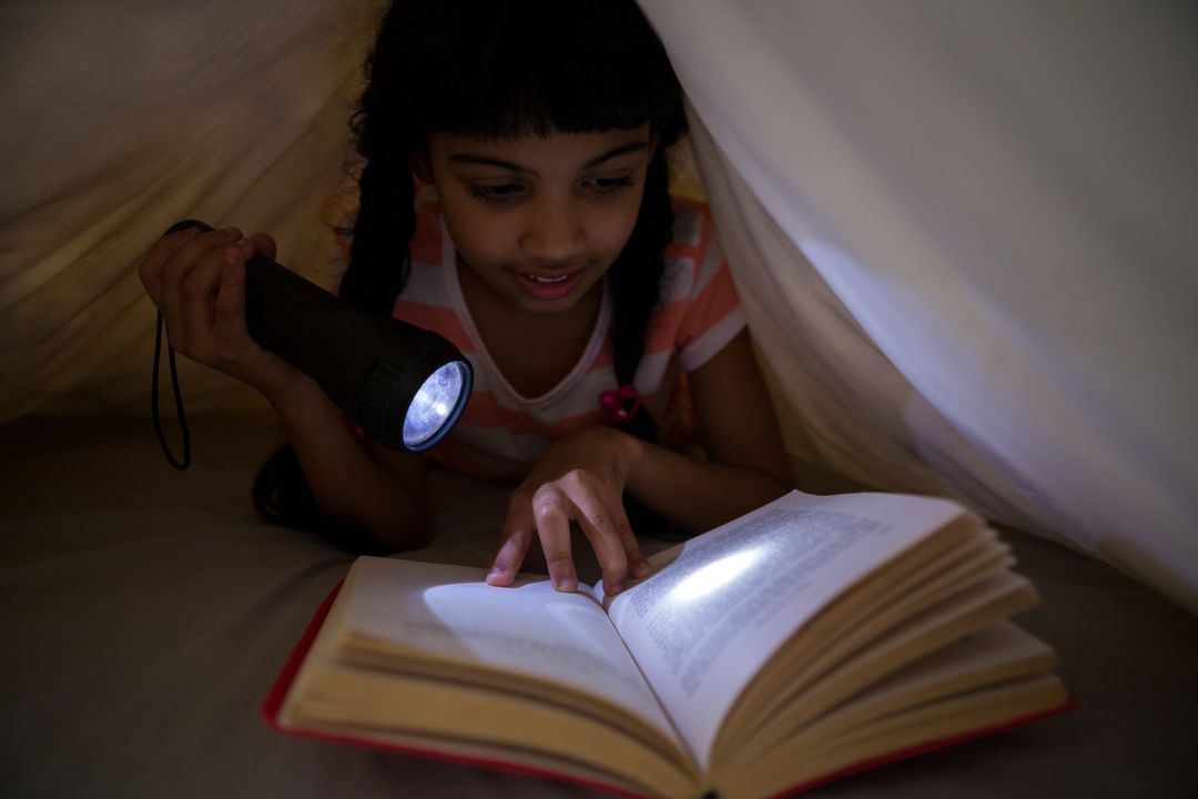Girl holding flashlight while reading novel under blanket - Free Images, Stock Photos and Pictures on Pikwizard.com