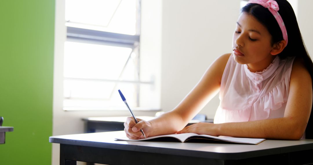 Young woman in sleeveless top studying at desk in brightly lit classroom - Free Images, Stock Photos and Pictures on Pikwizard.com