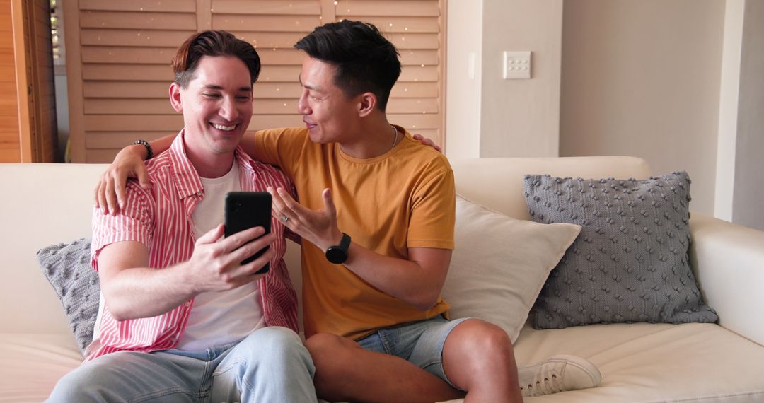 Diverse Male Couple Using Smartphone Joyously on Sofa at Home