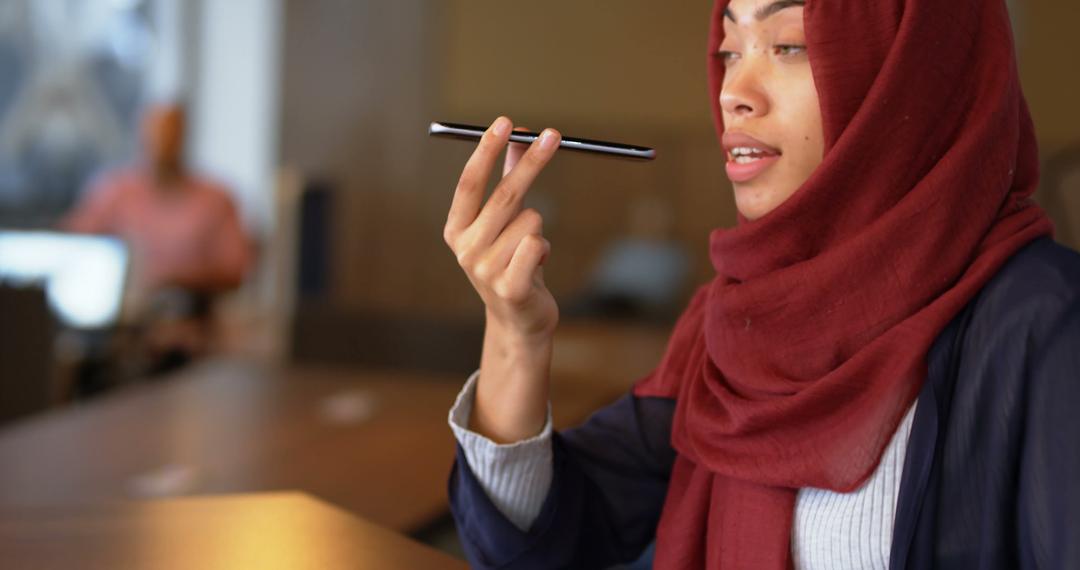 Young Muslim Woman Speaking Into Smartphone in Modern Office - Free Images, Stock Photos and Pictures on Pikwizard.com