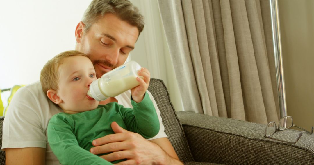 Father Feeding Toddler Son from Bottle in Cozy Living Room - Free Images, Stock Photos and Pictures on Pikwizard.com