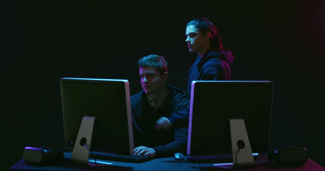 Two Men Collaborating at Computers in Dark Tech Environment