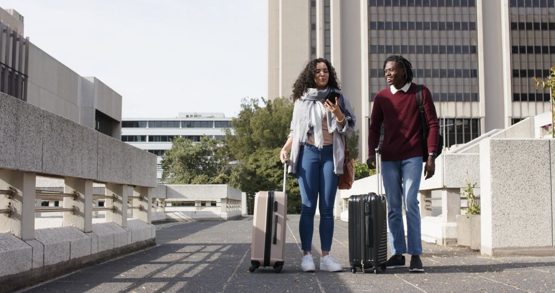 Diverse Young Couple Walking with Rolling Luggage on Walkway Daytime Using Smartphone