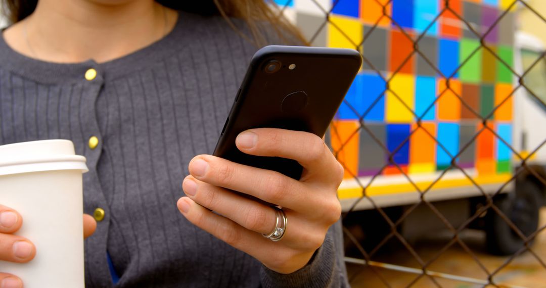 Person Holding Smartphone and Coffee Cup by Colorful Food Truck - Free Images, Stock Photos and Pictures on Pikwizard.com