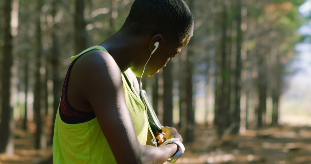 Young athlete adjusting music during outdoor exercise in forest - Free Images, Stock Photos and Pictures on Pikwizard.com