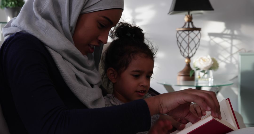 Mother in Hijab Reading with Daughter on Cozy Sofa