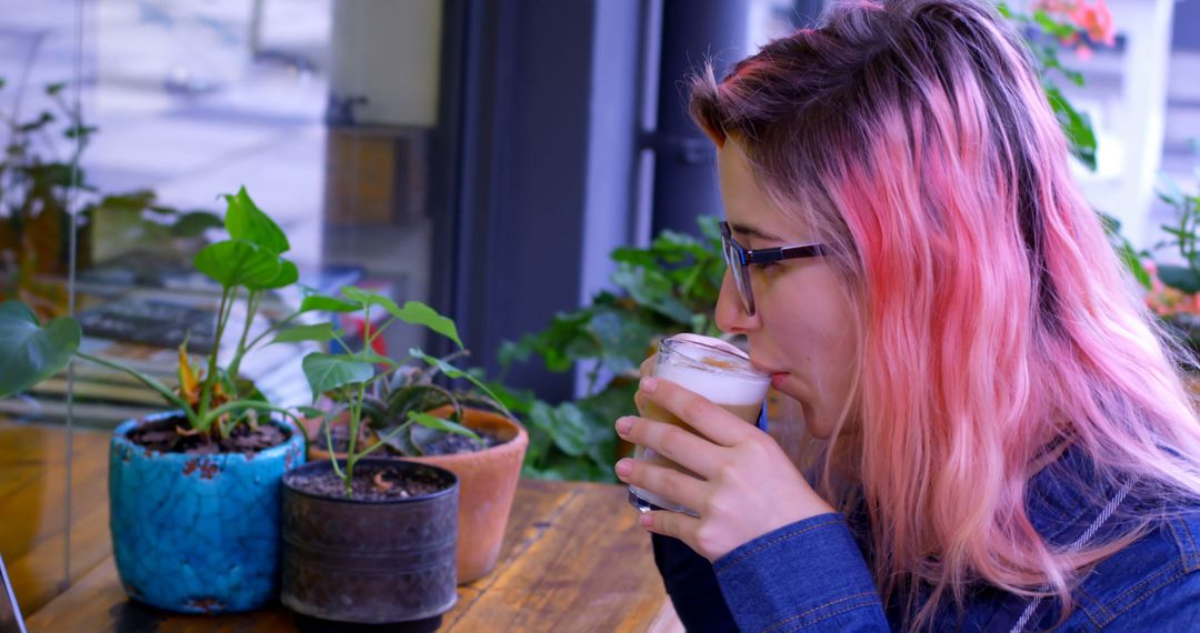 Young Woman with Pink Hair Enjoying Coffee Sit in Café by Plants - Free Images, Stock Photos and Pictures on Pikwizard.com