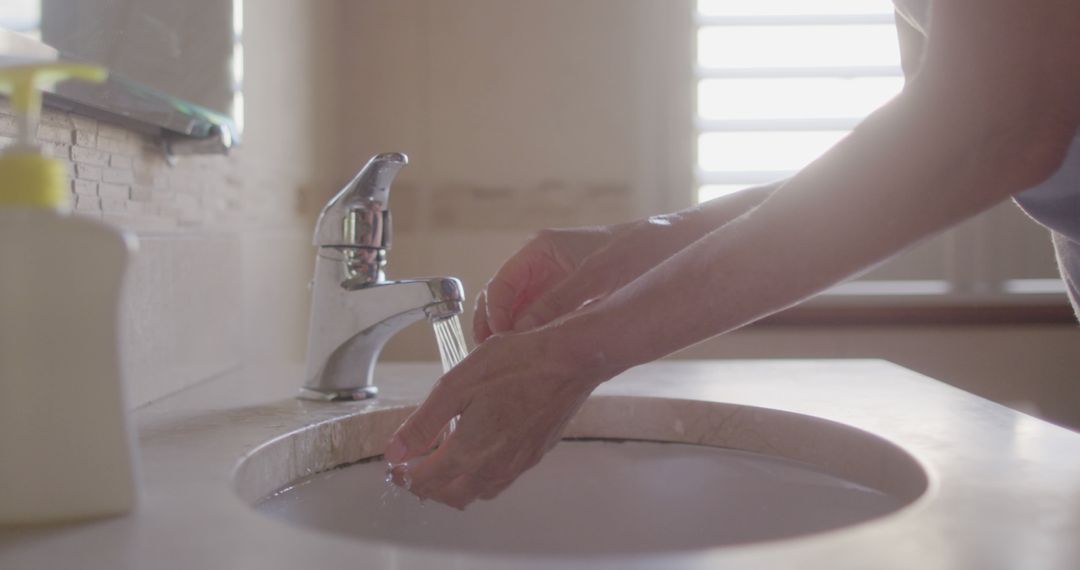 Senior Washes Hands with Tap Water in Sunlit Bathroom - Free Images, Stock Photos and Pictures on Pikwizard.com