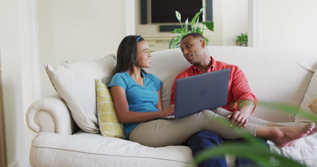 Happy Biracial Couple Relaxing on Sofa Using Laptop at Home