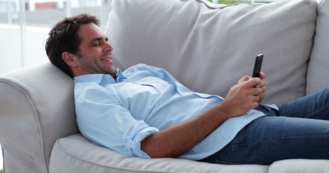 Smiling Man Relaxing on Couch While Using Smartphone at Home - Free Images, Stock Photos and Pictures on Pikwizard.com