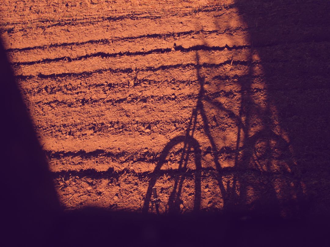 Bicycle shadow on textured dirt field at sunset - Free Images, Stock Photos and Pictures on Pikwizard.com