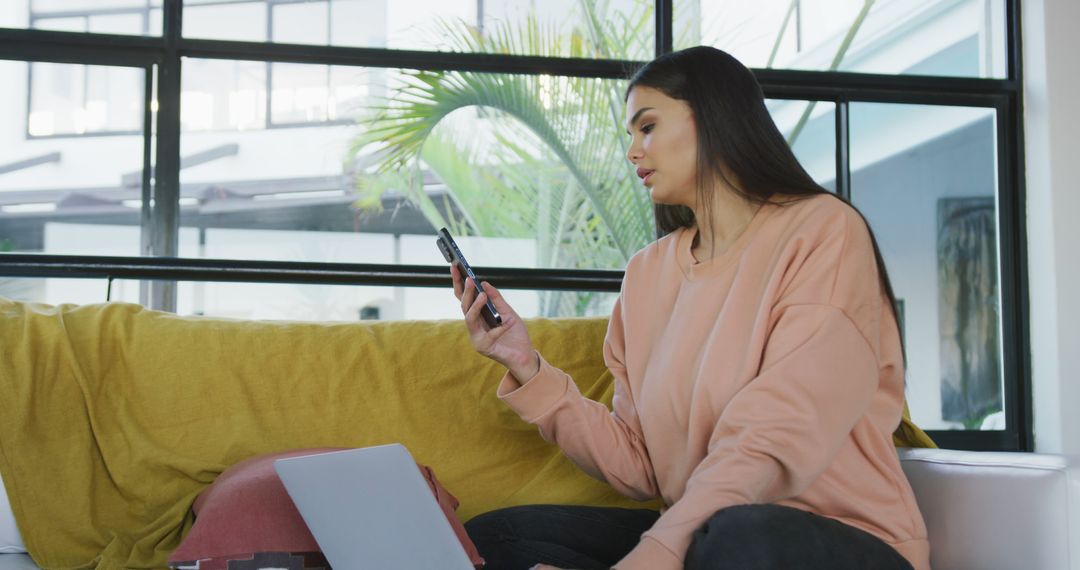 Image of happy biracial woman sitting on sofa and using smartphone - Free Images, Stock Photos and Pictures on Pikwizard.com