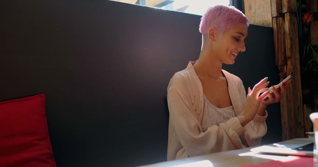 Woman with Pink Hair Smiling While Using Smartphone in Café - Free Images, Stock Photos and Pictures on Pikwizard.com