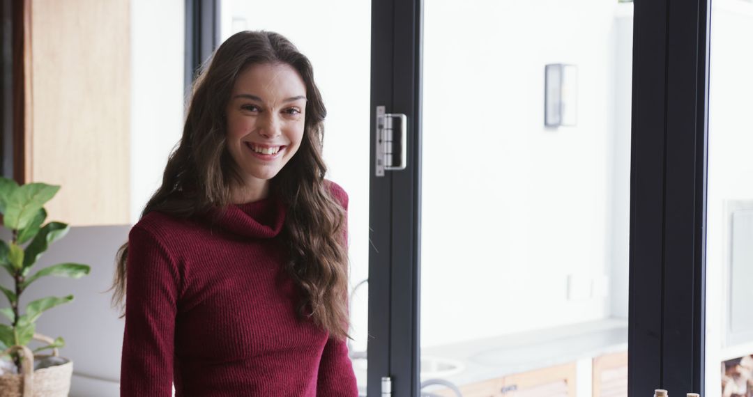 Smiling Woman with Long Hair in Red Sweater Standing by Window - Free Images, Stock Photos and Pictures on Pikwizard.com