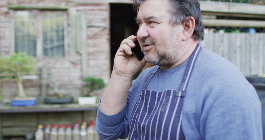 Middle-aged man in apron talking on phone outdoors - Free Images, Stock Photos and Pictures on Pikwizard.com