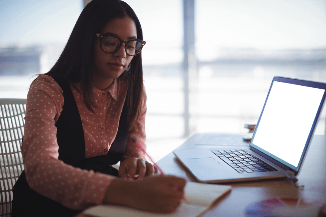Focused Young Businesswoman in Creative Office Setting with Laptop and Notebook