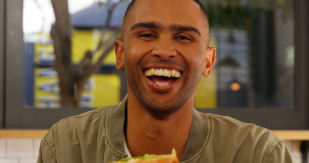 Man Happily Laughing While Holding Big Sandwich Inside Cafe - Free Images, Stock Photos and Pictures on Pikwizard.com