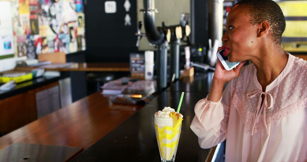 Woman Drinking Milkshake While Talking on Phone in Modern Cafe - Free Images, Stock Photos and Pictures on Pikwizard.com