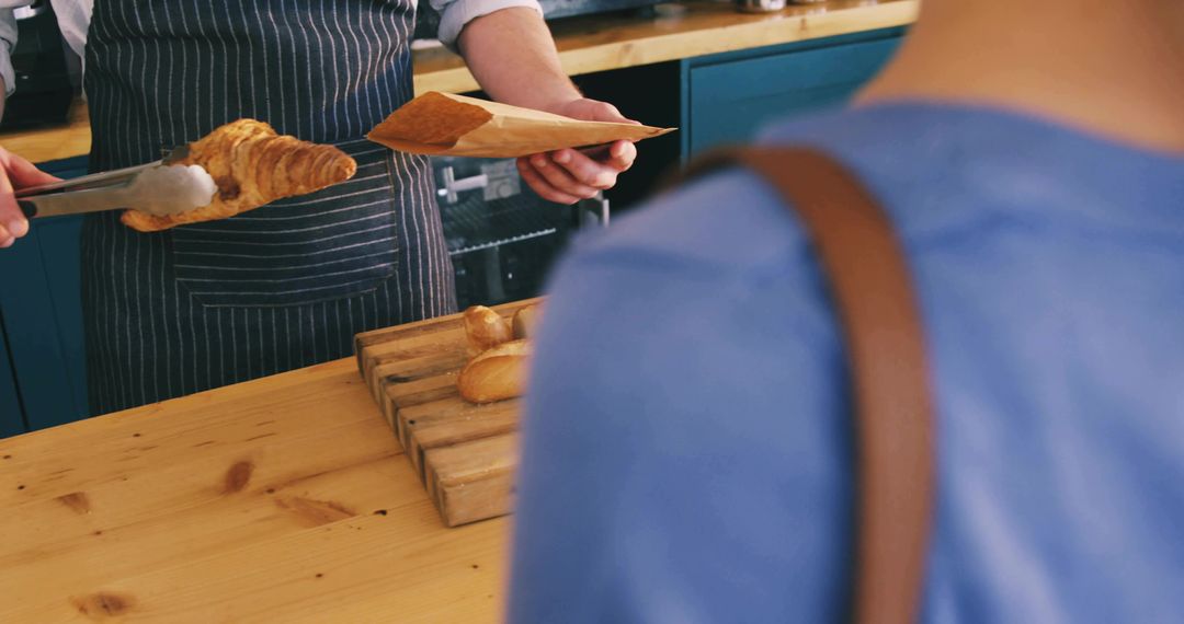 Serving fresh croissant with tongs at rustic bakery counter from customer view