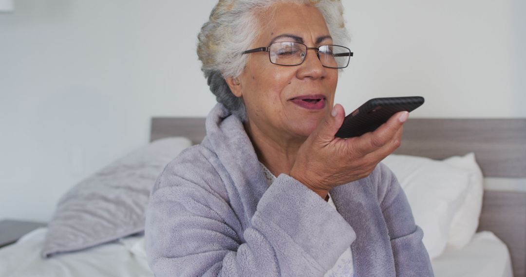 Elderly Woman Using Voice Command on Smartphone While Sitting in Bed - Free Images, Stock Photos and Pictures on Pikwizard.com