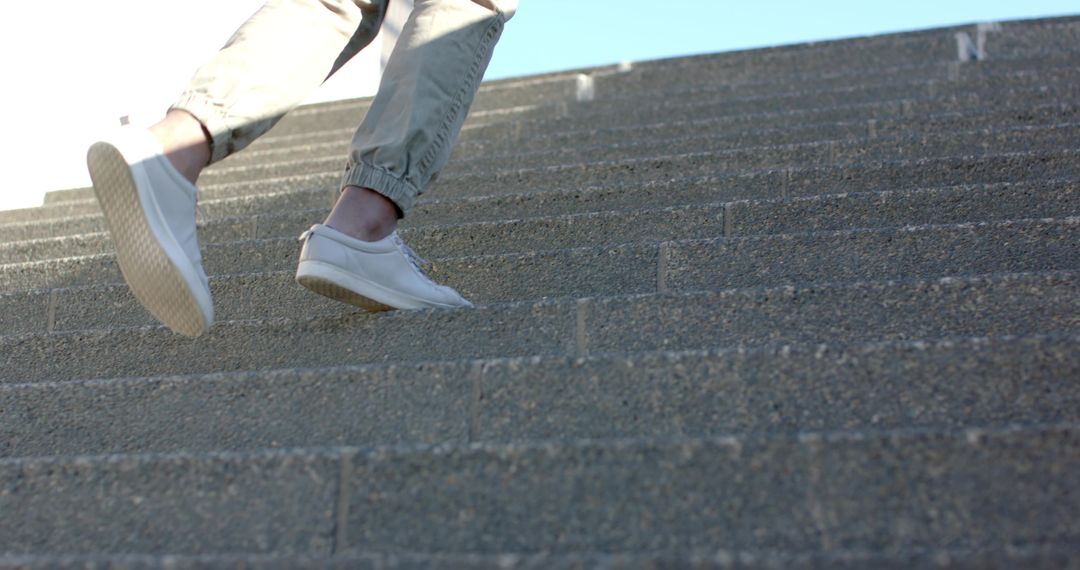 Ascending concrete steps wearing white sneakers and cuffed pants, urban motion and texture