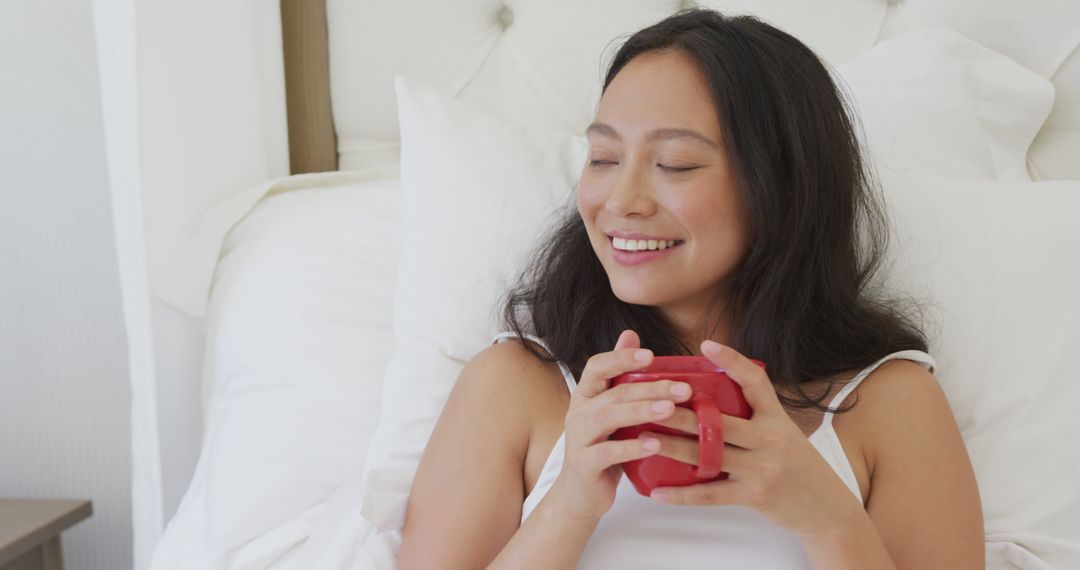 Smiling Asian Woman Relaxing in Bed with Warm Drink - Free Images, Stock Photos and Pictures on Pikwizard.com