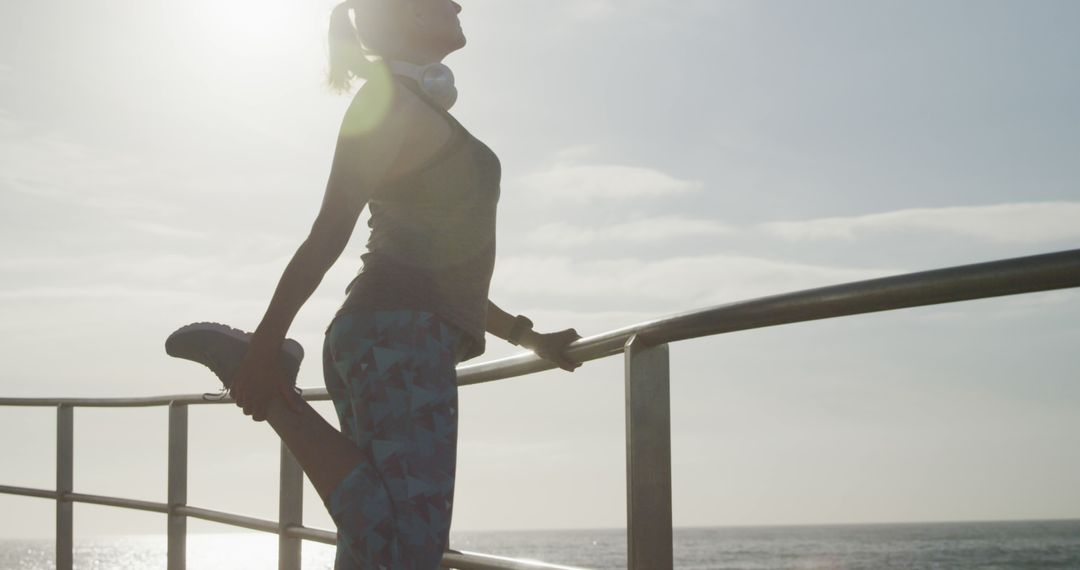 Woman stretching legs on oceanfront promenade during sunset - Free Images, Stock Photos and Pictures on Pikwizard.com