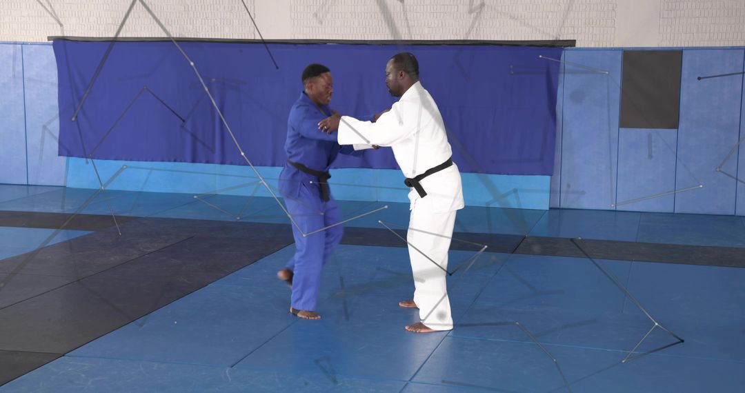 Two Judokas Grappling in White and Blue Gis on Padded Mats Black Belts Practicing Throws