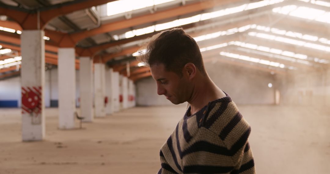 Man Standing in Empty Industrial Warehouse Wearing Striped Sweater - Free Images, Stock Photos and Pictures on Pikwizard.com