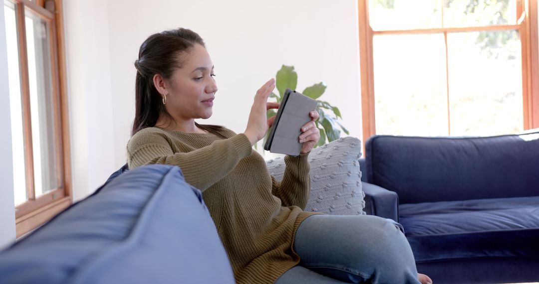 Young woman using digital tablet on blue sofa at home - Free Images, Stock Photos and Pictures on Pikwizard.com