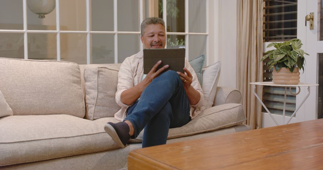 Senior Man Relaxing on Sofa Using Tablet for Leisure at Home