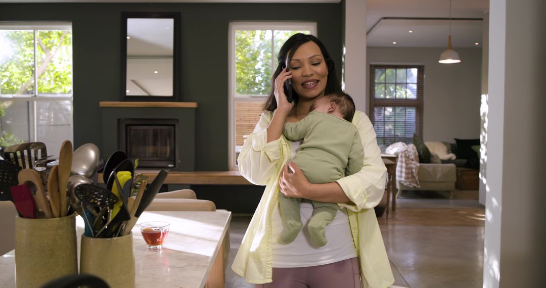 Mother Speaking on Smartphone While Holding Baby in Cozy Kitchen
