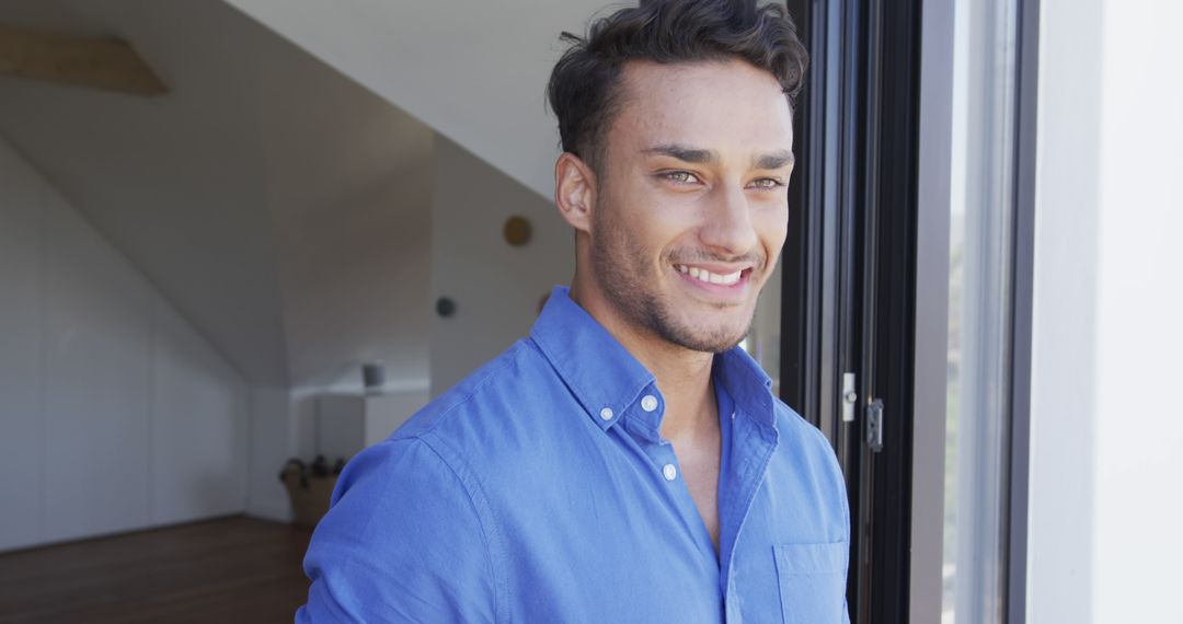 Smiling Young Man in Blue Shirt Standing by Window - Free Images, Stock Photos and Pictures on Pikwizard.com