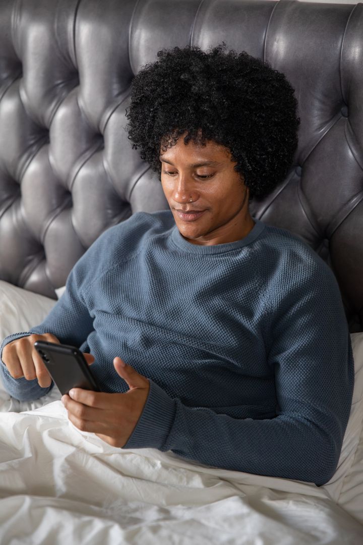 Man Relaxing with Smartphone on Chic Bed, Modern Lifestyle Theme