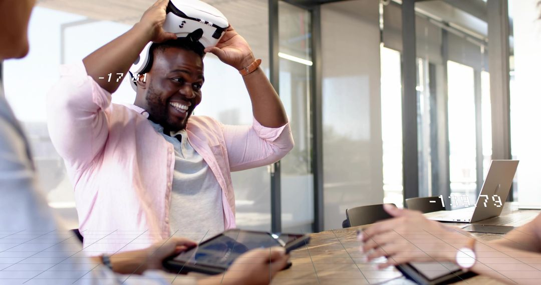 Smiling man putting on white VR headset during collaborative meeting in modern office