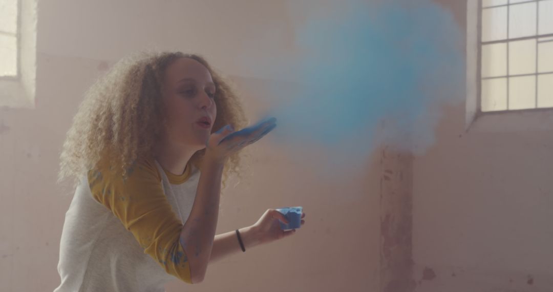 Playful Woman Blowing Blue Powder Indoors - Free Images, Stock Photos and Pictures on Pikwizard.com