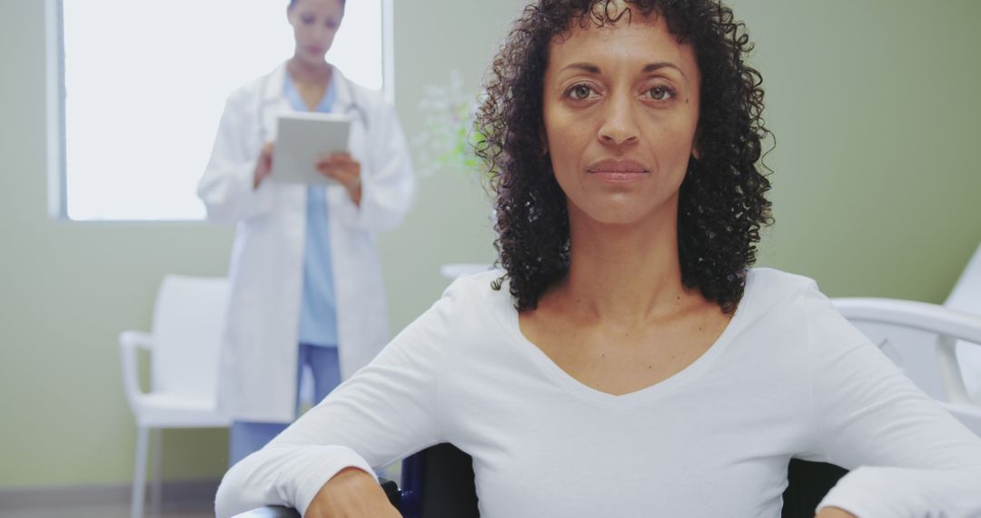 Confident Woman Sitting in Hospital with Doctor in Background - Free Images, Stock Photos and Pictures on Pikwizard.com